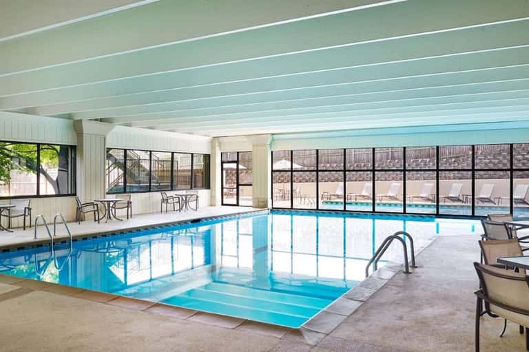 Indoor heated swimming pool with large windows overlooking outdoor pool deck