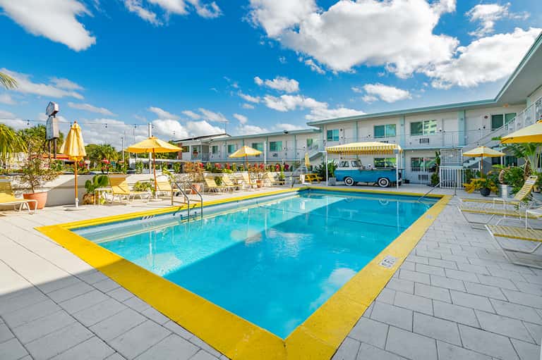 Retro-style motel pool with blue water, yellow trim, and mid-century building facade