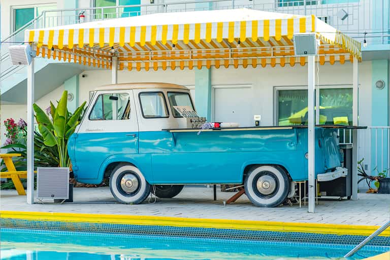 Vintage blue and white food truck under yellow striped awning by resort pool