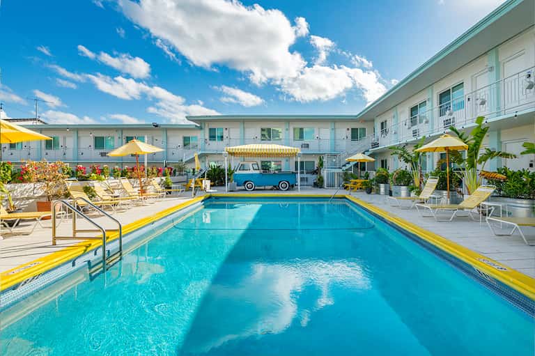 Vintage-style motel courtyard with swimming pool, yellow umbrellas, and classic American architecture