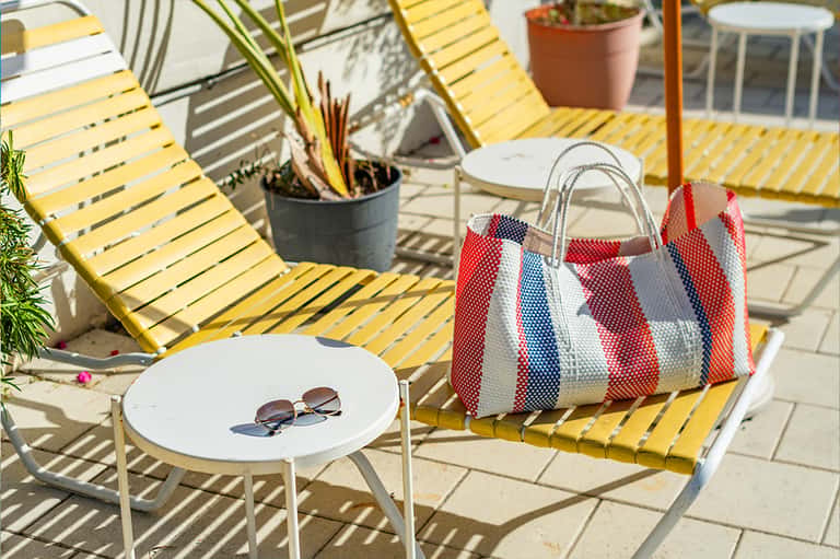 Sunny rooftop deck with yellow lounge chairs, potted plants, white side table, and patterned beach bag