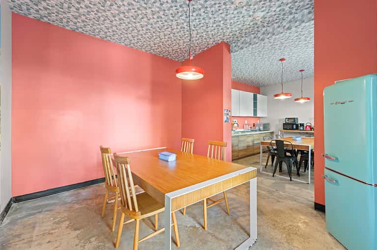 Retro-style kitchen and dining area with coral pink walls, turquoise refrigerator, and patterned ceiling