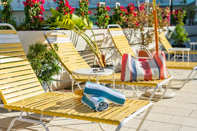 Rooftop deck with yellow lounge chairs, flowering vines, and beach bags in sunlight