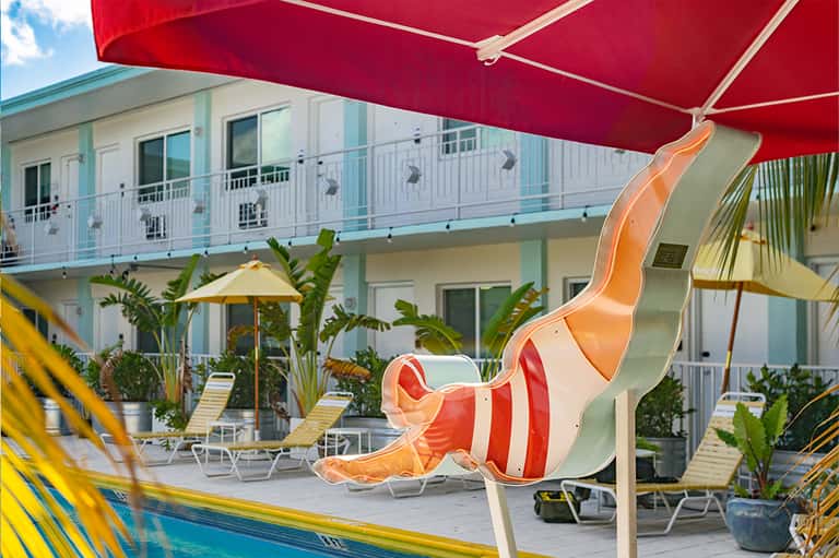 Resort pool area with red umbrellas, water slide, and tropical landscaping