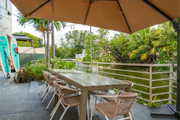 Waterfront deck with dining table, umbrella, palm trees, and water view