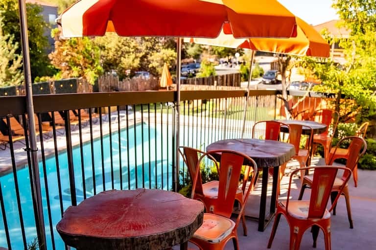 Poolside patio with red umbrellas, tables, and lush greenery