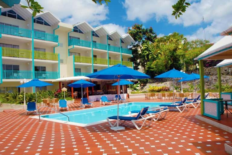 Resort pool area with bright blue umbrellas, lounge chairs, colorful building with turquoise accents