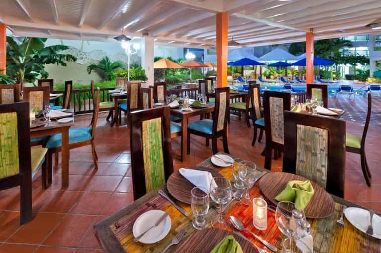 Indoor restaurant dining area with wooden furniture, colorful umbrellas, and pool view outside