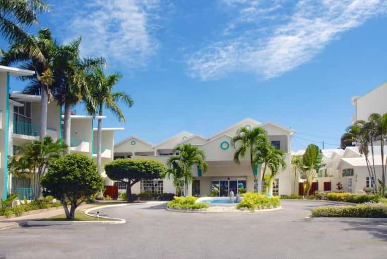 Tropical resort entrance with white buildings, palm trees, turquoise accents, and manicured landscaping