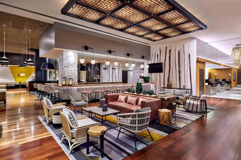 Upscale hotel lobby with bar, lounge seating, decorative pendant lights, and modern geometric ceiling design.