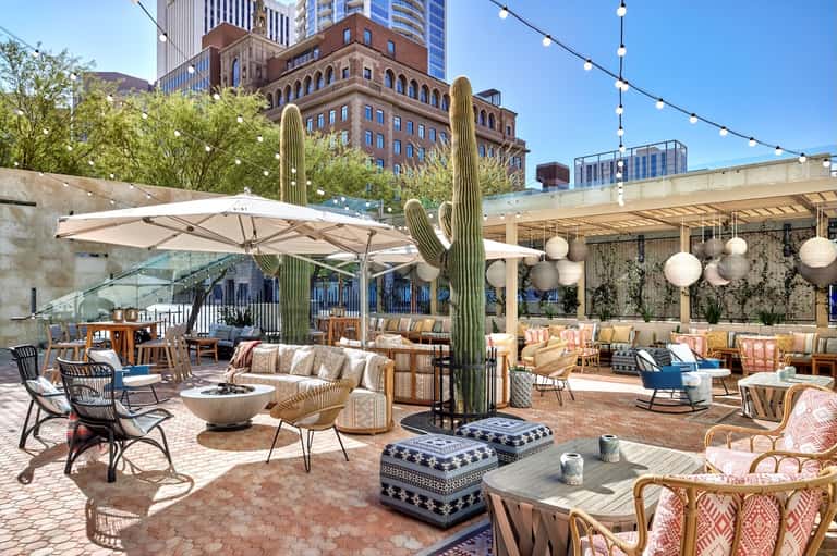 Upscale rooftop lounge with saguaro cactus, umbrellas, fire pit, and contemporary seating areas