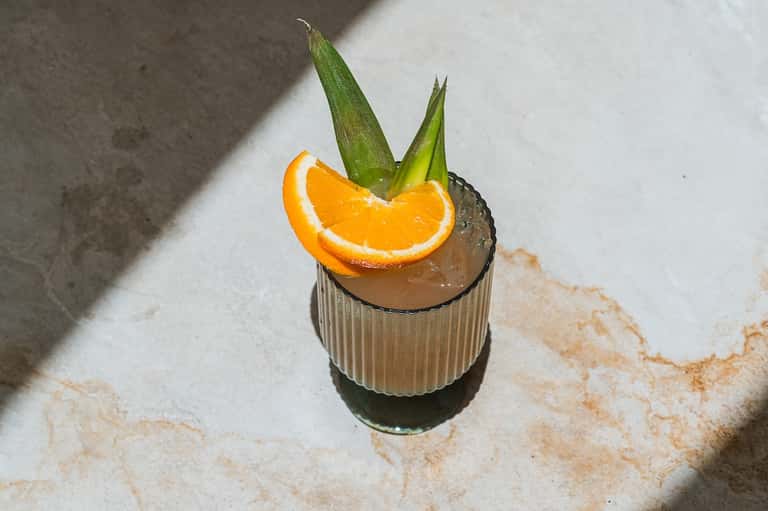 Tropical cocktail with orange slice and green leaves on concrete resort deck in sunlight