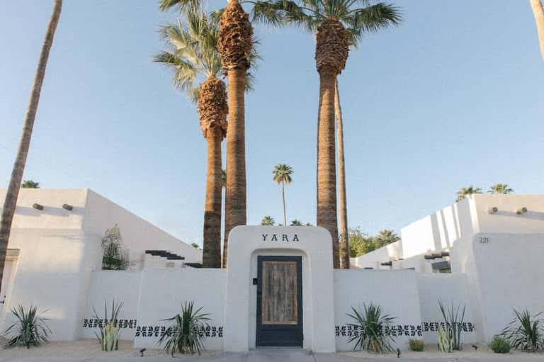 Modern minimalist white building entrance with tall palm trees and clear skies