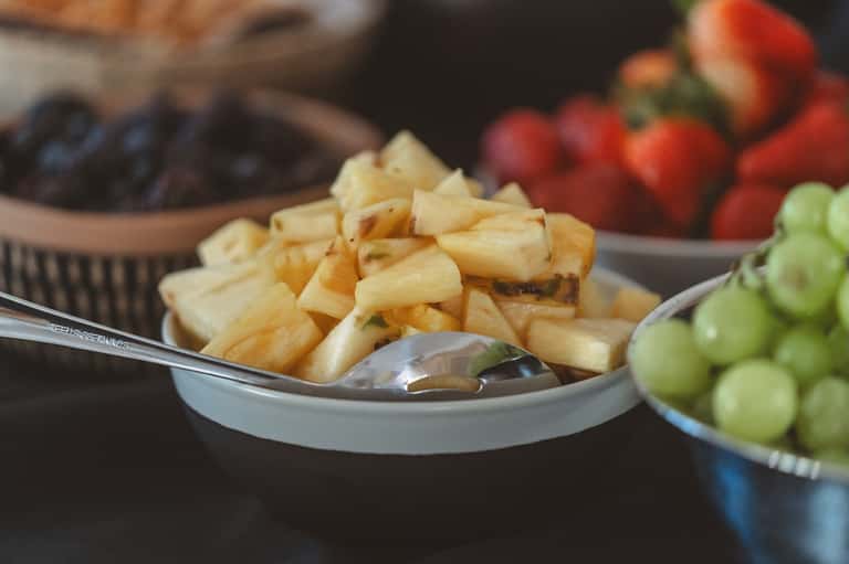 Close-up of appetizers including cheese cubes and fresh fruits arranged on white serving plates