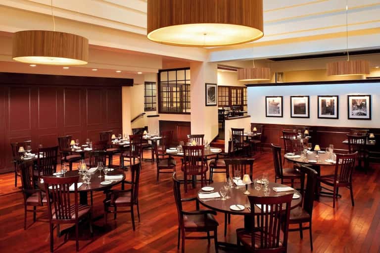 Upscale restaurant dining room with mahogany wood, round tables, and framed artwork