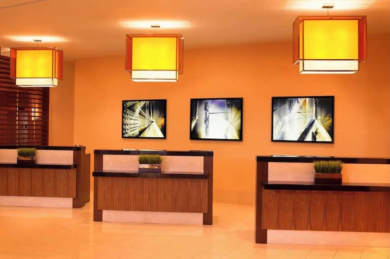 Hotel lobby with orange walls, wooden reception desks, and modern lighting