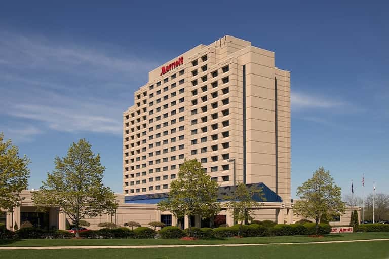 Exterior of a tan Marriott hotel tower with manicured landscaping against a blue sky
