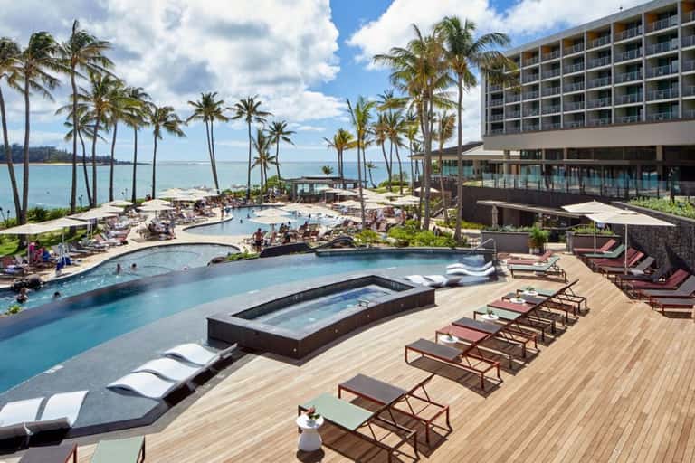 Beachfront resort pool complex with palm trees, ocean view, spa, and high-rise building