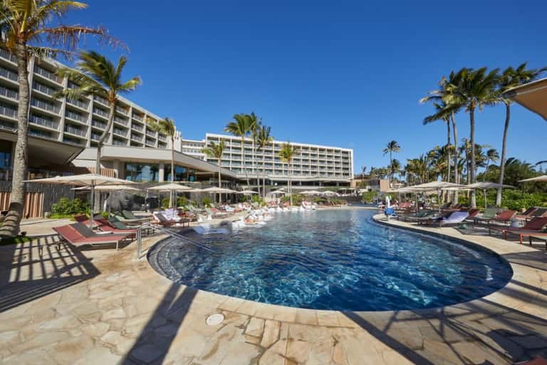 Resort pool with curved edges, loungers, umbrellas, and palm trees near hotel building