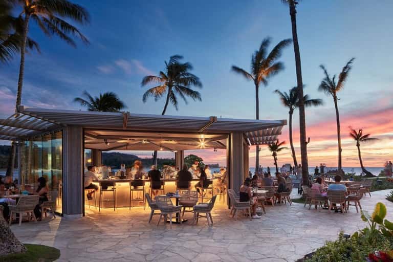 Sunset beachside bar and lounge with palm trees, modern seating, and ocean views at dusk