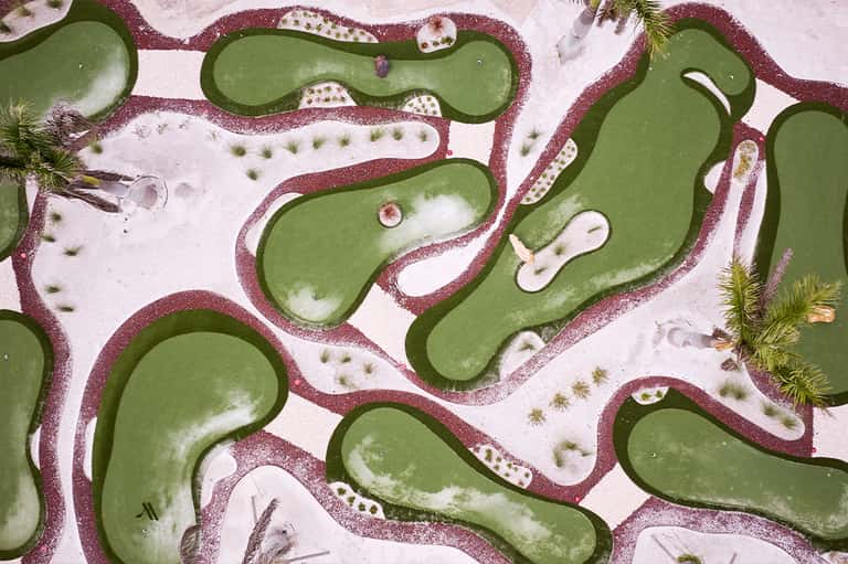 Aerial view of miniature golf course with curved green fairways bordered by burgundy sand