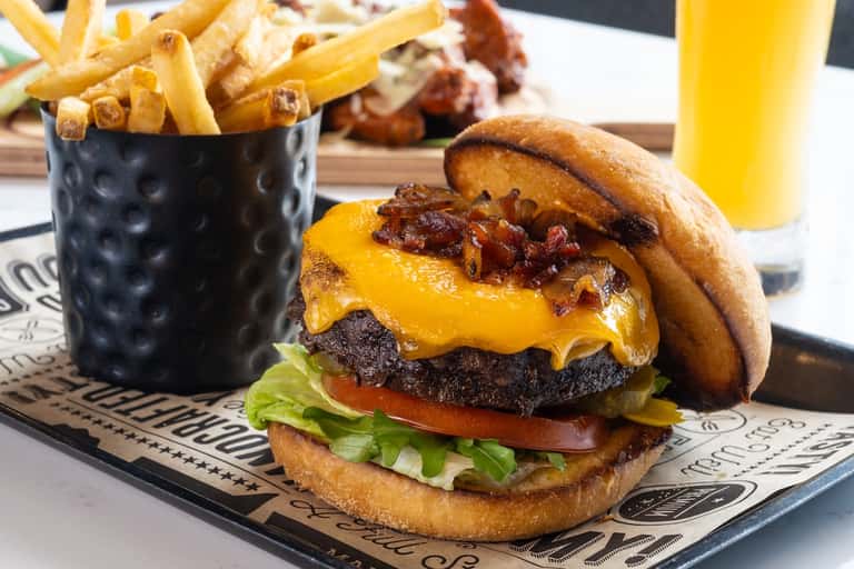 Gourmet cheeseburger with bacon and fries served on branded placemat with beverage