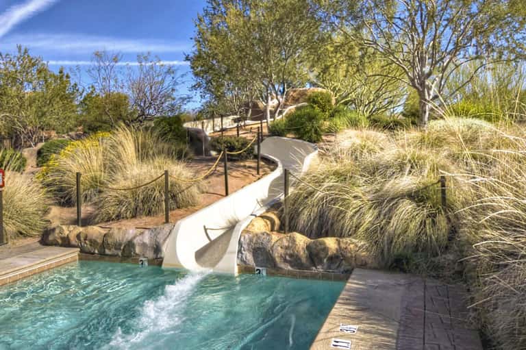 Water slide into turquoise pool surrounded by ornamental grasses and wooden deck