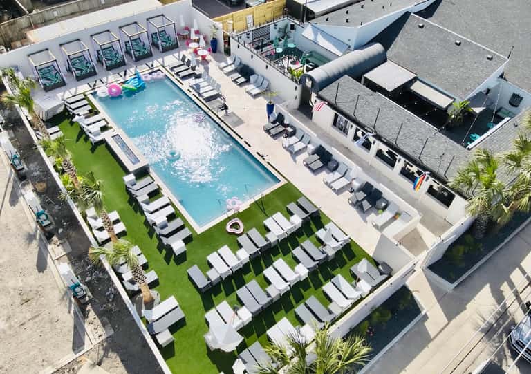 Aerial view of resort pool deck with white lounge chairs, green lawn, and modern buildings