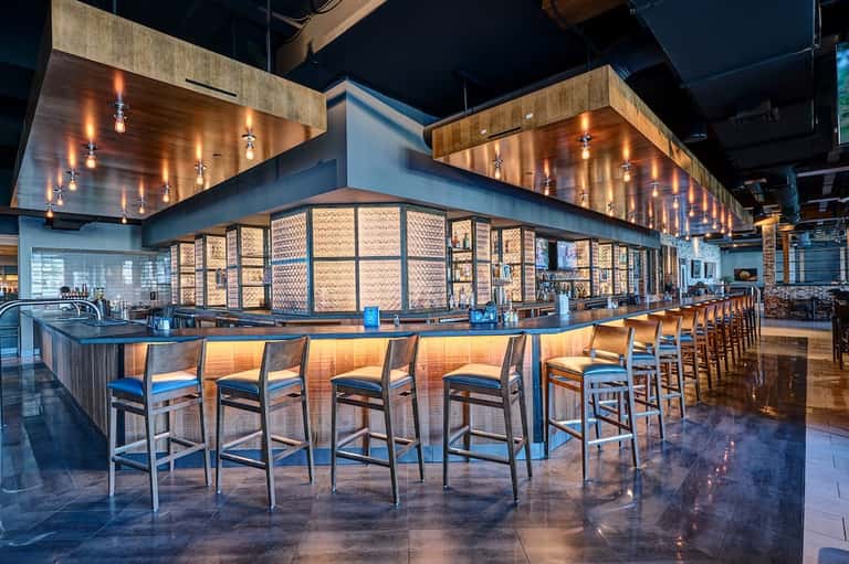 Contemporary hotel bar with wooden ceiling, illuminated central bar with stools, and modern design