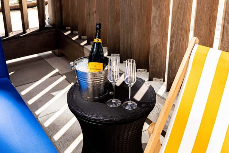 Champagne bottle in ice bucket with glasses on round table in wooden cabana