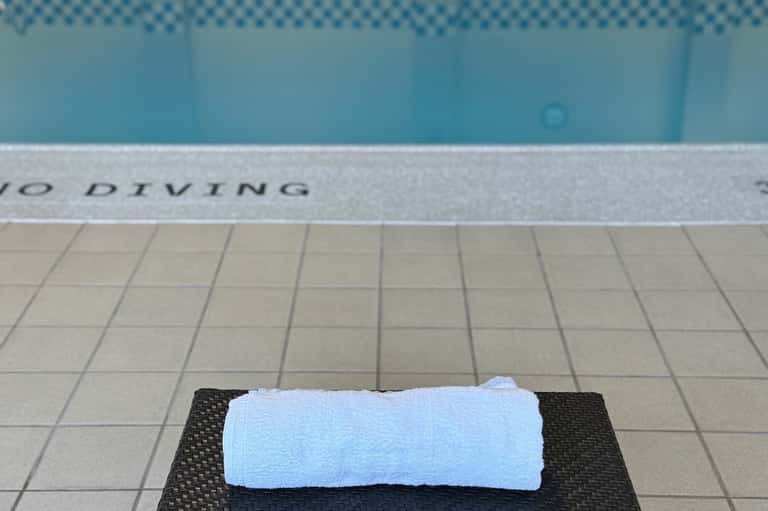 White towel on dark mat beside a pool with "NO DIVING" text visible on deck edge