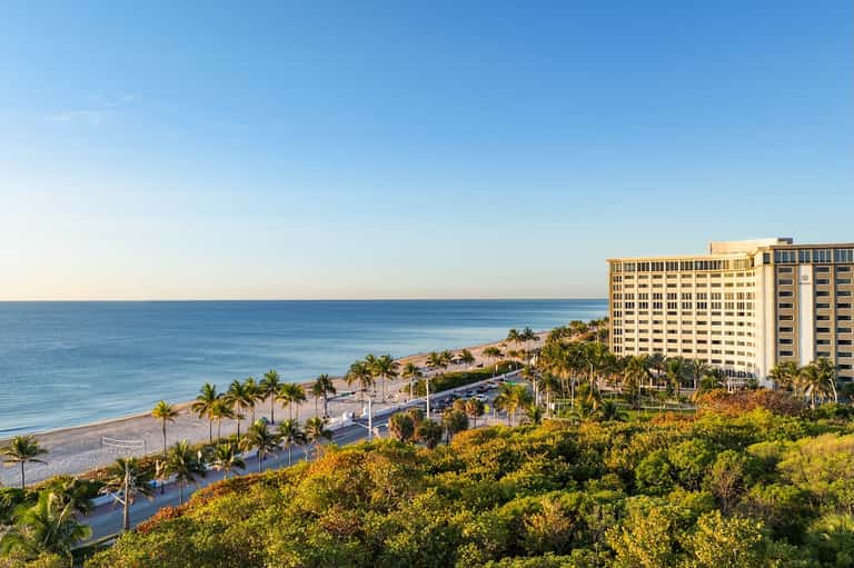 Beachfront resort hotel overlooking sandy beach, palm trees, and calm blue ocean waters