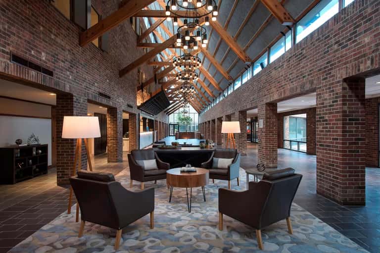 Modern hotel lobby with exposed brick, wooden beams, chandeliers, and contemporary seating areas