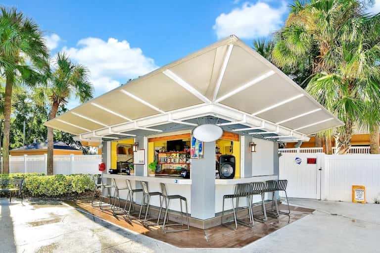 Casual outdoor bar with retractable awning, palm trees, and white picket fence