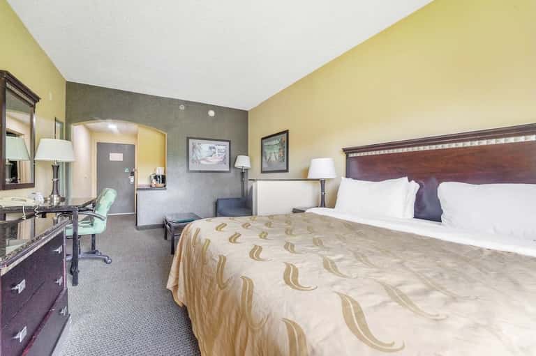 Hotel bedroom with queen bed, work desk, yellow and gray walls, and bathroom entrance