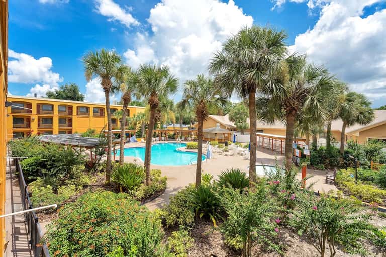 Resort courtyard with swimming pool, tall palm trees, yellow building, and lush landscaping