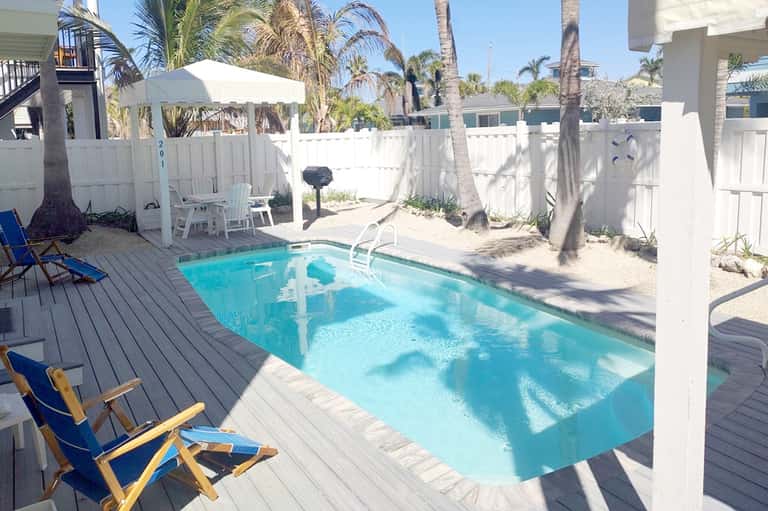 Beach cottage private pool with wooden deck, palm trees, white fence, and lounge chairs