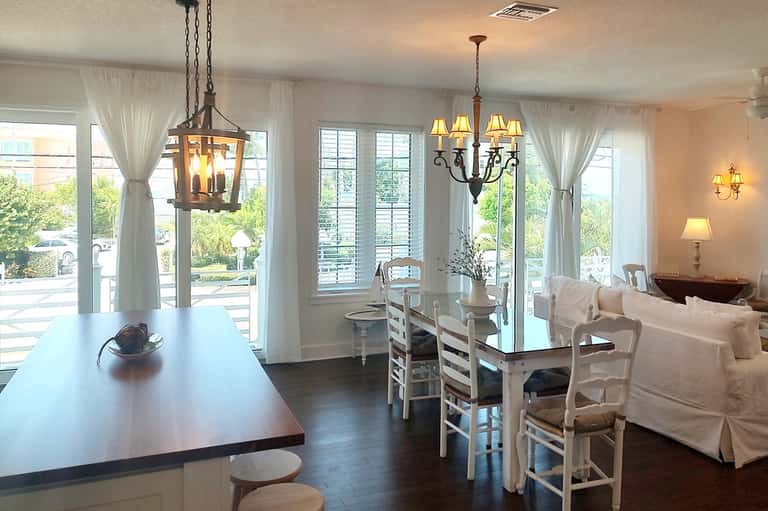 Elegant interior living space with chandeliers, white furniture, dark flooring, and large windows