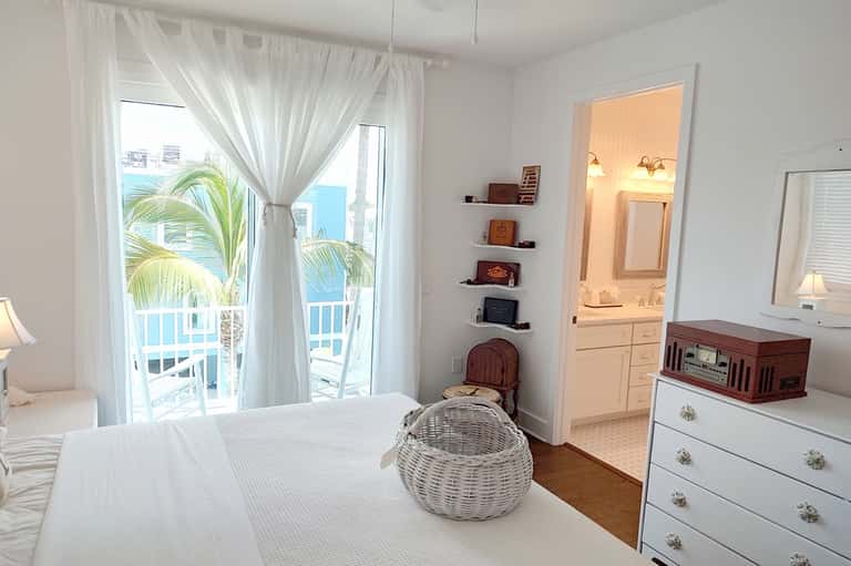 Beachfront bedroom with ocean view, white bed, palm tree views from balcony, and en-suite bathroom