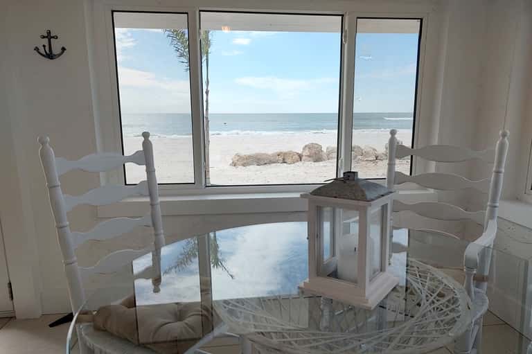 Bright beachfront room interior with glass doors overlooking sandy beach and ocean horizon