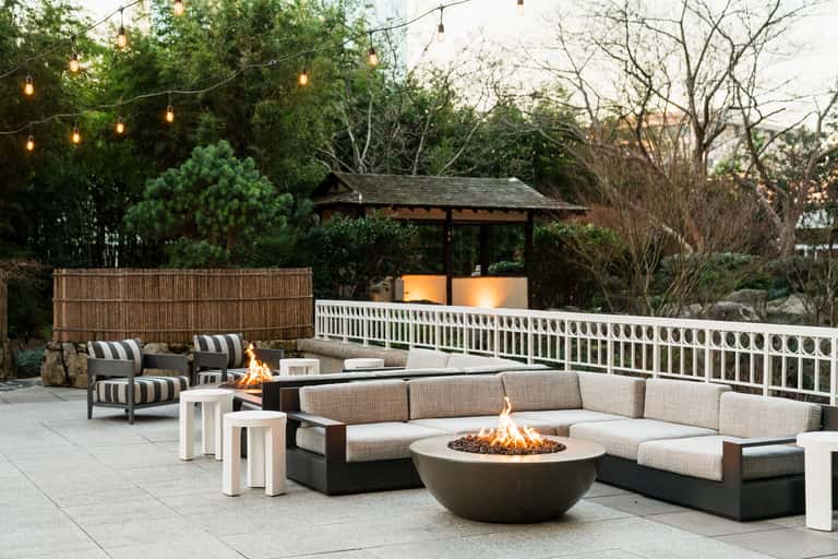 Outdoor patio with fire pit, modern lounge seating, hanging string lights, pergola, and landscaping