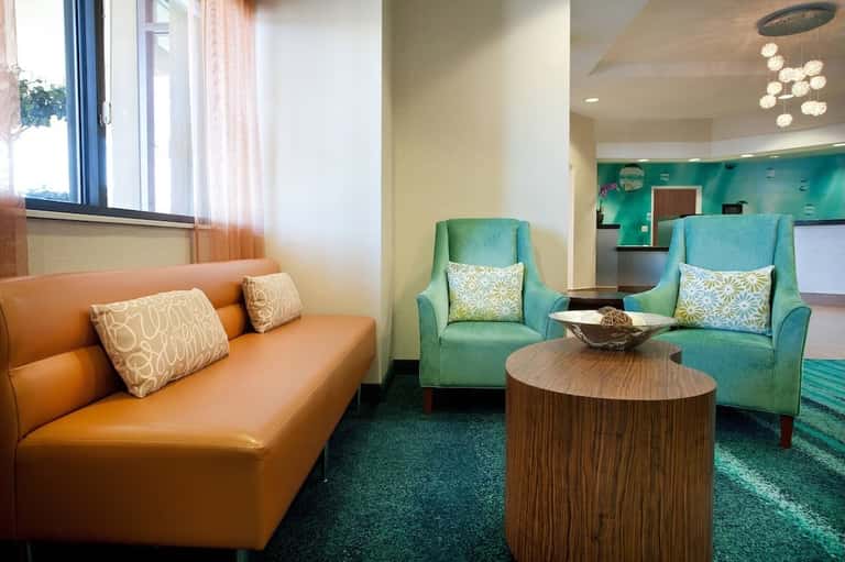 Contemporary hotel lounge with orange sofa, turquoise armchairs, wood table, and teal accent wall