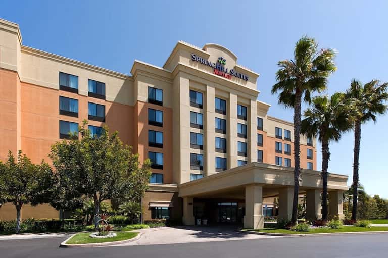 Modern hotel exterior with orange and cream facade, palm trees, clear sky, and covered entrance