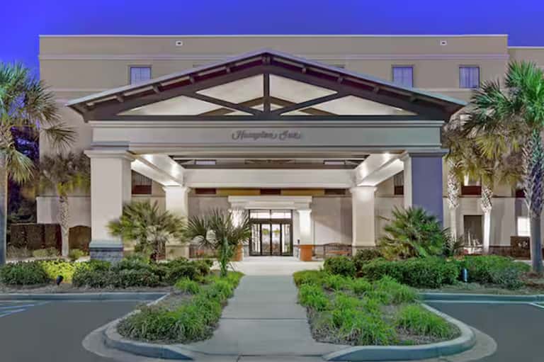 Hampton Inn hotel entrance with white columns, dark roof, and manicured landscaping at dusk