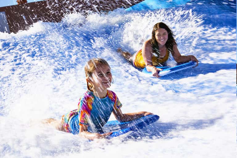 Young girl and woman playing in ocean waves with boogie boards on sandy beach