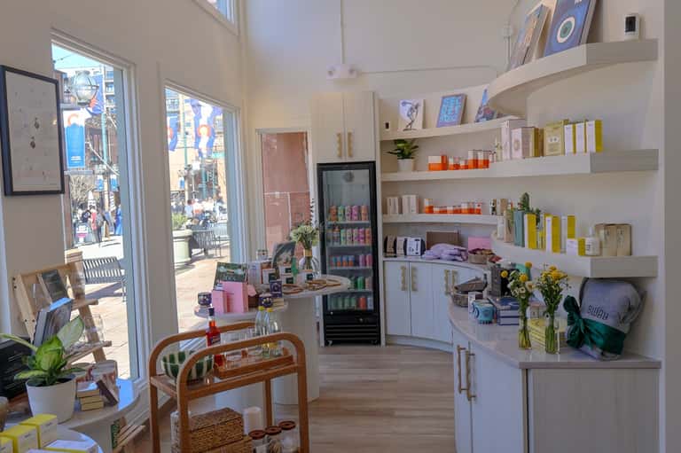 Bright spa retail shop interior with white shelving, products, refrigerator, and outdoor views through windows
