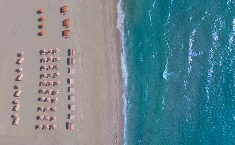 Aerial beach view with organized rows of umbrellas, loungers, and ocean waves