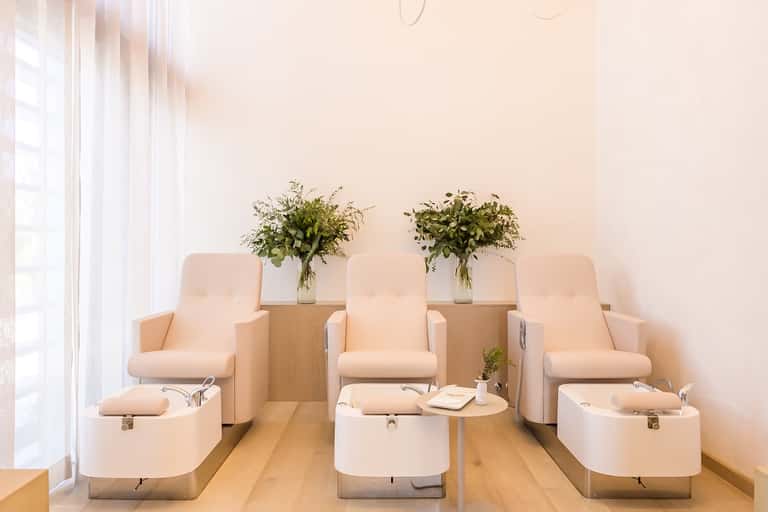 Spa pedicure area with three white massage chairs and fresh flower arrangements on wood tables