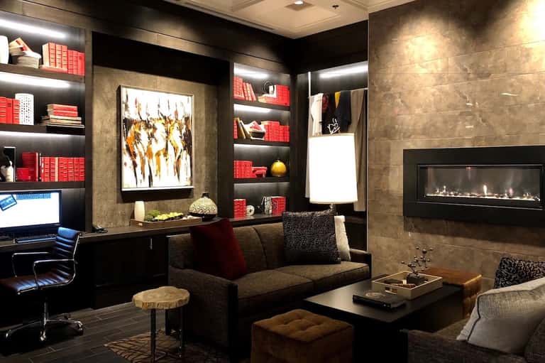 Luxury office lounge with fireplace, red-accented shelving, artwork, and modern seating