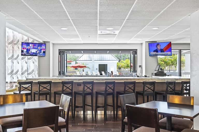 Hotel bar and lounge area with seating, counter, TV screens, and views to outdoor patio space